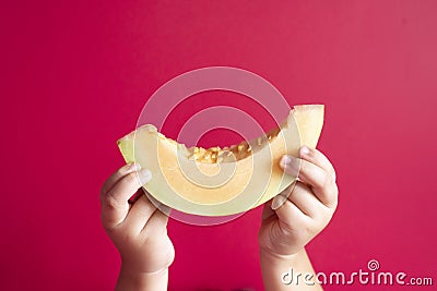 Little child hand holding a honeydew melon or rockmelon against pink background. Stock Photo