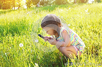 Little child looking through a magnifying glass on dandelion Stock Photo