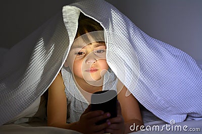 Little child play on smart phone in bed under the covers at nigh Stock Photo