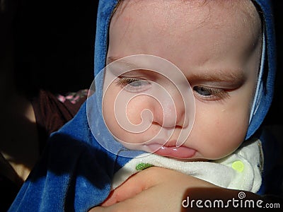 The little child pouted and frowned. Tired or sleepy look to the side. Plump kid with thick cheeks. On the boys head is a hood Stock Photo