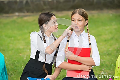 Little child in school uniform touch skin of girl classmate sitting on park bench, skincare Stock Photo