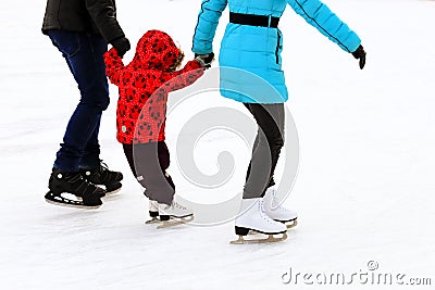 Little child skates with his parents at the ice rink in winter. A man and woman is teaching her child to skate. Sports clubs Stock Photo