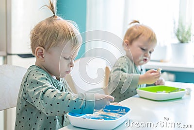 Little children blonde boys twins in pajamas hungry eating healthy food in kitchen at home Stock Photo