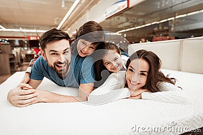 Little children lie on the backs of young happy parents in a mattress store. Stock Photo