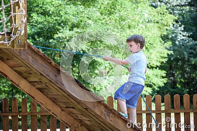 Little climber takes the rope bridge. Boy has fun time, kid climbing on sunny warm summer day Stock Photo