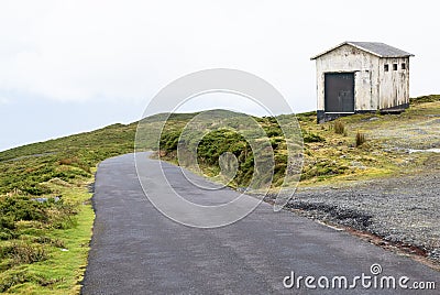 Little concrete hut on roadside with green hills, road, and sky Stock Photo