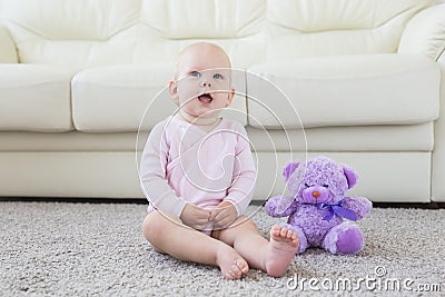 Little crawling baby girl one year old sitting on floor in bright light living room smiling and laughing. Happy toddler Stock Photo