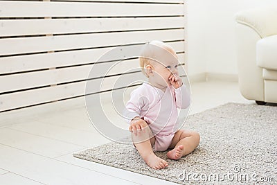 Little crawling baby girl one year old sitting on floor in bright light living room smiling and laughing. Happy toddler Stock Photo