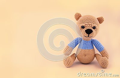 Little crocheted teddy bear on a gentle yellow background. Soft toy handmade. Stock Photo