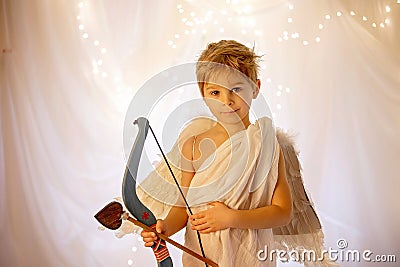 Little cupid toddle boy, holding bow and arrow, beautiful blond cherub Stock Photo