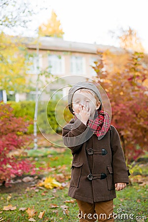 Little cute boy in an autumn coat and cap plays in an autumn park with yellow leaves Stock Photo