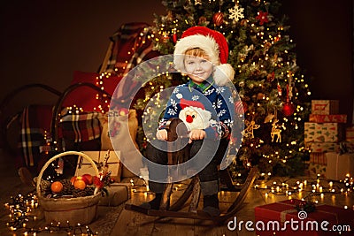 Little Cute Boy in Christmas Decorated Room Interior. Child on vintage wooden Toy Horse. Christmas tree with rustic ornament Stock Photo