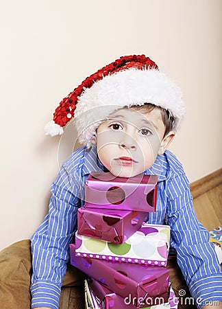 Little cute boy with Christmas gifts at home. close up emotional face on boxes in santas red hat Stock Photo