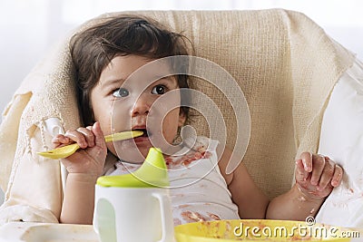 Little child celebrating her first birthday with cake at home. Baby adorable girl with apron holding spoon in her hand while Stock Photo