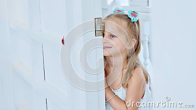 Little cute child girl peeks through the doorway in room with funny emotions Stock Photo