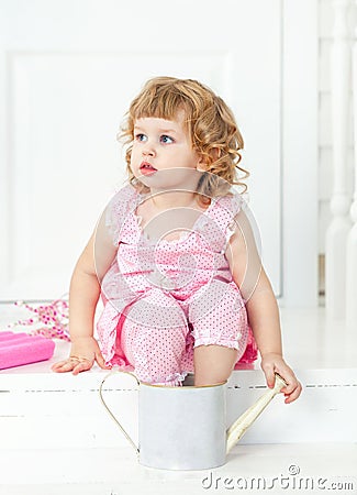 Little cute curly girl in a pink dress with polka dots sitting on the white porch Provence style Stock Photo