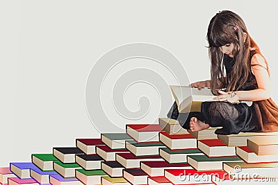 A wise little cute girl kid in a black dress sitting on pile of book reading and learning knowledge and information Stock Photo