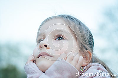 A little cute girl with long hair is sitting in a park seriously sad Stock Photo