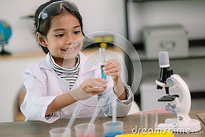 Little cute girl with a microscope holding a laboratory bottle with water experiment study scientists at school. Education science Stock Photo