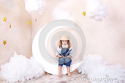 Little cute girl sitting on the moon with clouds and stars with a book in her hands and reading. The girl is learning to read. Rea Stock Photo