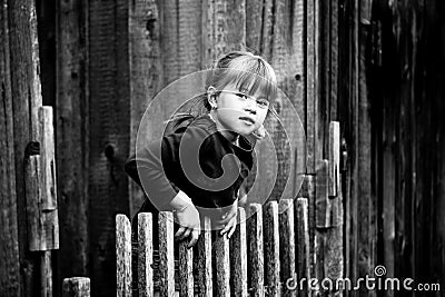 Little cute girl standing near vintage rural fence. Black and white photography. Stock Photo