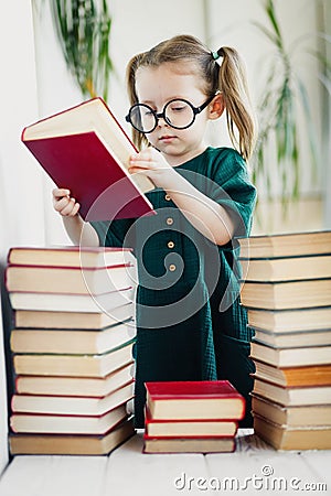 Little cute kid girl in glasses with pile of books, vertical Stock Photo