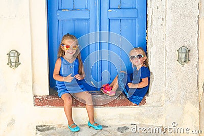 Little cute sisters sitting near old blue door in Stock Photo