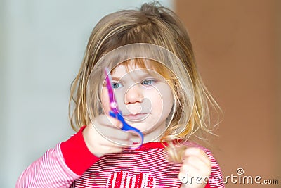 Little cute toddler girl making experiment with scissors and cutting hairs. Funny baby child cuts her pony herself at Stock Photo