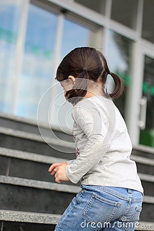 little cute white brunette girl with ponytails climbs up the stairs Stock Photo