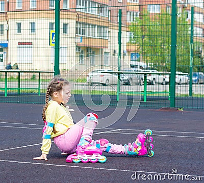 A little cute white girl in a yellow sweatshirt and pink jeans on roller skates in the park. Learn to rollerblade Stock Photo