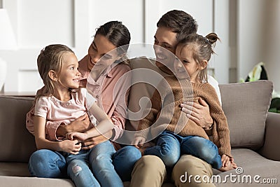 Little daughters sit on parents laps talking resting on couch Stock Photo