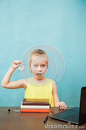 Little elementary age girl homeschooling with books, laptop and alarm clock. Stock Photo