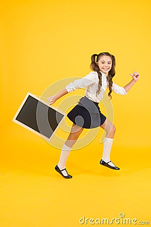 Little and energetic. Little child carrying blackboard on yellow background. Little schoolgirl with black-board for Stock Photo