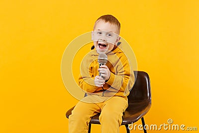 Little fun kid boy 3-4 years old in yellow clothes sing song in microphone isolated on bright orange wall background Stock Photo