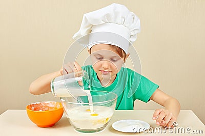 Little funny chef pours milk for baking cake Stock Photo