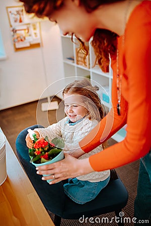 Little funny daughter watering home flowers with mother Stock Photo