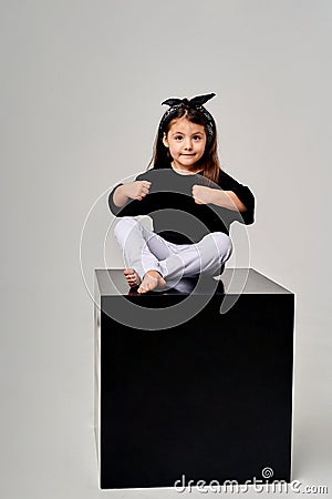 little funny girl sitting on a black cube on a white background Stock Photo