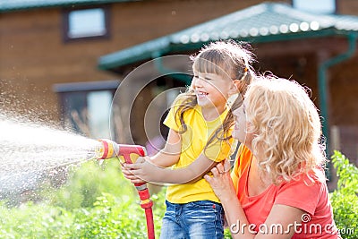Little gardener girl with mother watering on lawn Stock Photo
