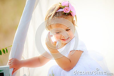 Little girl adjusts her hair of hut for games. Child with beautiful hairstyle in white dress. Stock Photo