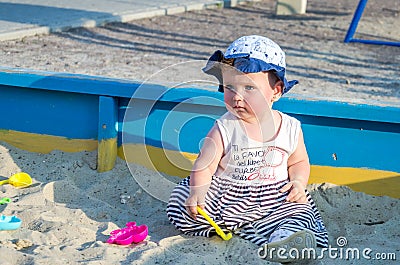 Little girl baby in a cap plays with toys in a sandbox with sand on the playground Stock Photo