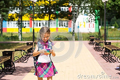Little girl with a backpack and in a school uniform in the school yard plays pop it toy. Back to school, September 1. The pupil Stock Photo