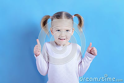 A little girl with blond hair shows a super gesture with two hands. Photo of a funny baby on a light blue background. Stock Photo