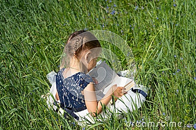 Little girl with a book in the garden. Kid is readding a book. A little girl 4-5 years old sits on the grass and reads a book Stock Photo