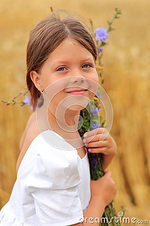 Little girl with a bouquet of wildflowers in her hands in a wheat field. Stock Photo
