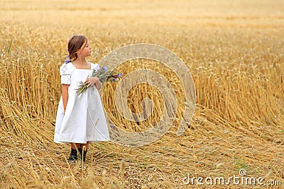 Little girl with a bouquet of wildflowers in her hands in a wheat field. Stock Photo