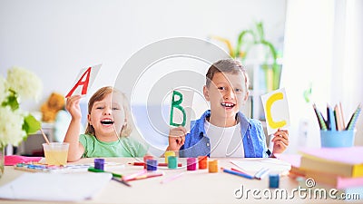 A little girl and a boy learn at home. happy kids at the table with school supplies smiling funny and learning the alphabet in a Stock Photo