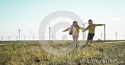 Little girl and boy are running in front of windmills. Renewable energies and sustainable resources - wind mills Stock Photo