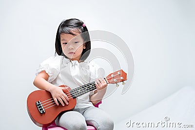 Little girl with brown ukulele toy gift. Child learn to play strum instruments Stock Photo