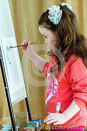 Little girl with a brush at the easel thinks about the future drawing. Beautiful model 4-5 years Stock Photo