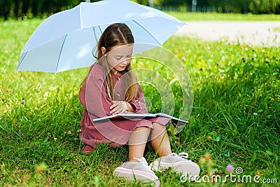 Little girl in dress reading book in park Stock Photo